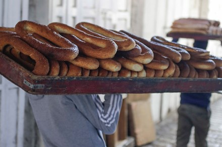 From behind, two people carry huge trays full of ring-shaped bread on their shoulders.