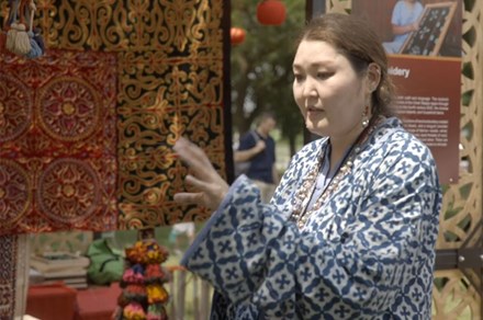 A woman in a blue and white patterned dress gestures with one hand.