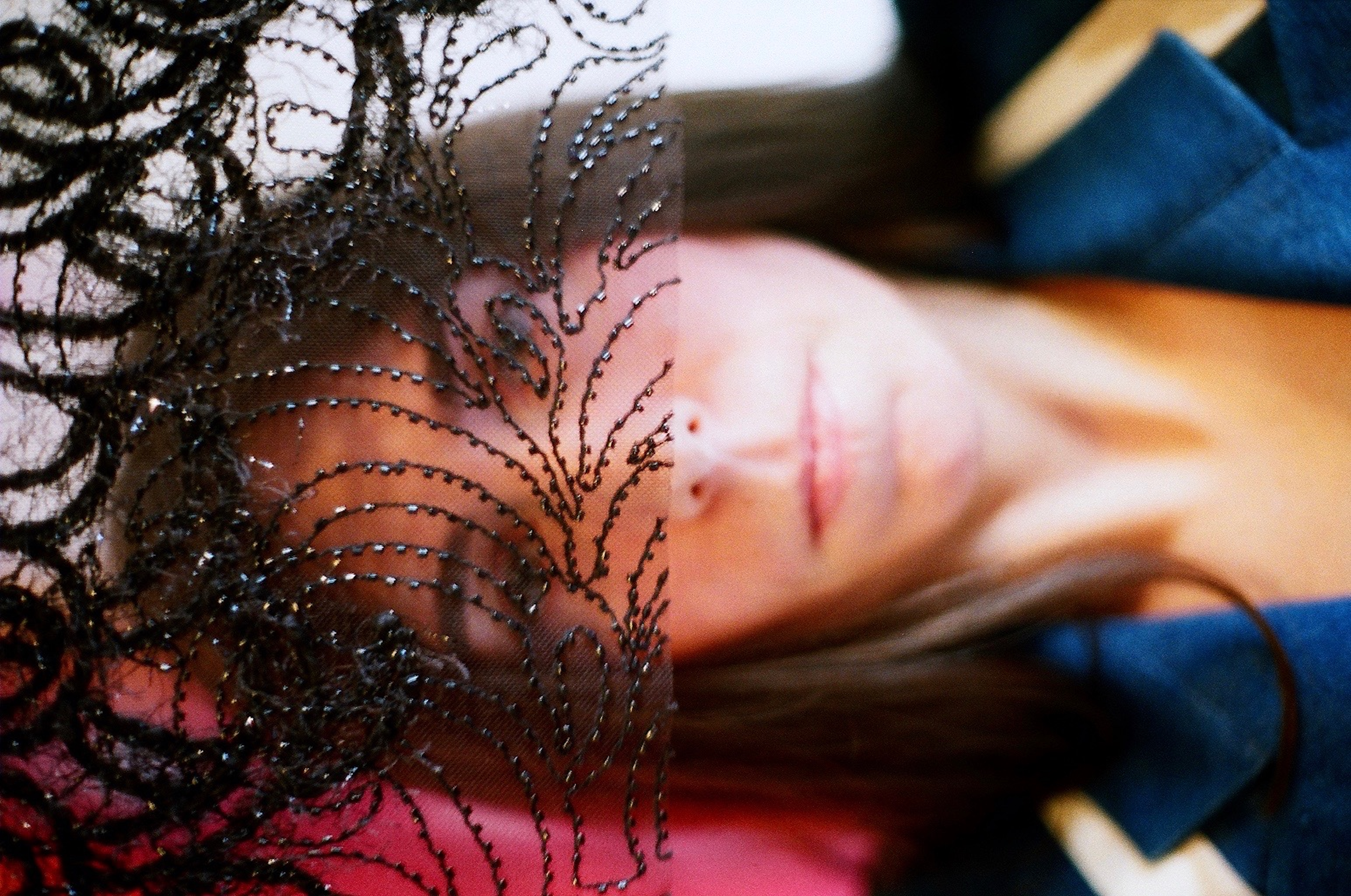 Portrait of a woman with long dark hair, sideways, holding up a piece of black lace that covers the top half of her face.