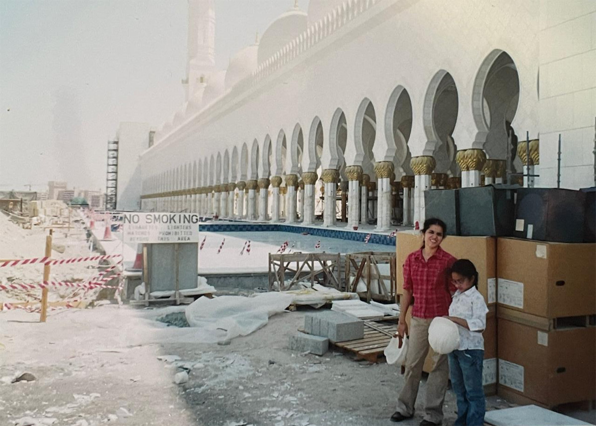 A young girl and mother in the foreground on the right. Behind them, signs and construction cones. In the far background, another building is obscured by dusty air.