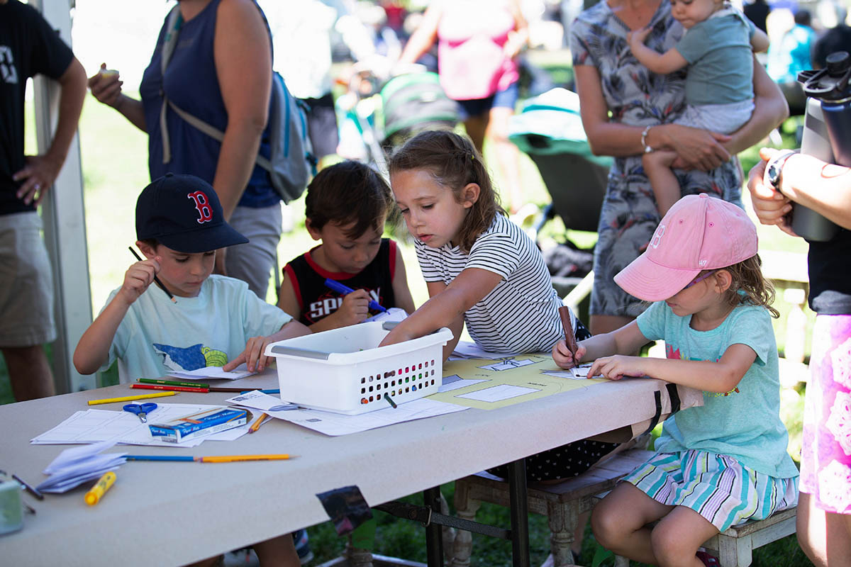 Four children sitting at a table, using colored pencils to draw on paper.