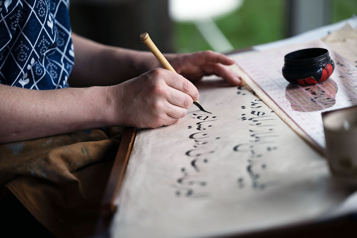 Close-up on a pair of hands as someone writes Arabic calligraphy with a stylus.