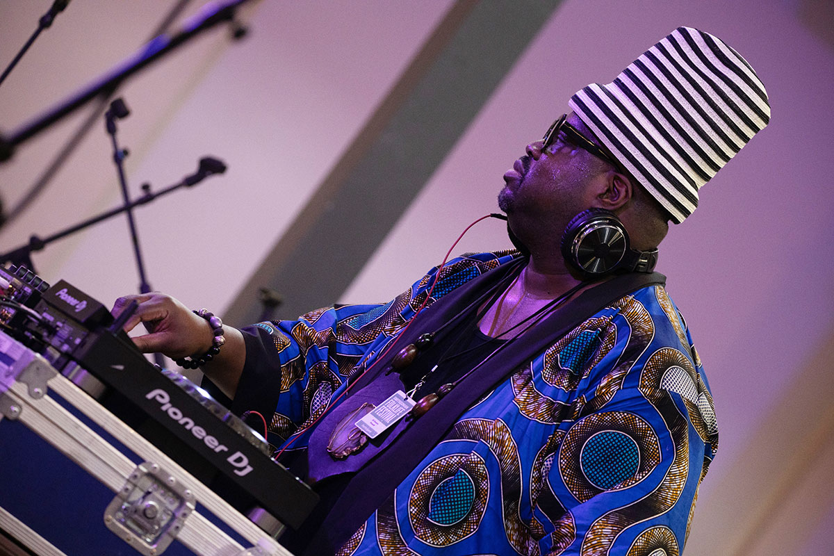 A DJ wearing a flowing blue top and tall, cylindrical white and black striped hat.