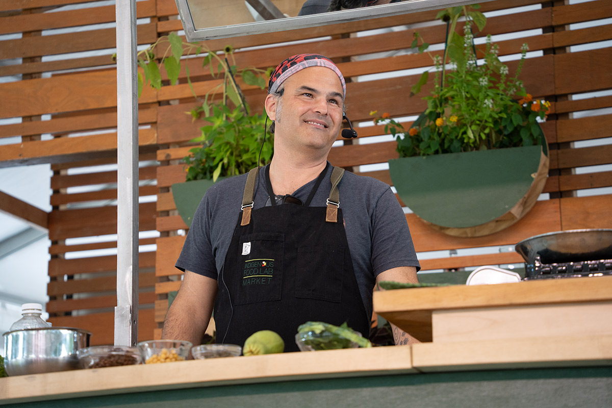 A man wearing a red bandana and a black apron that reads 