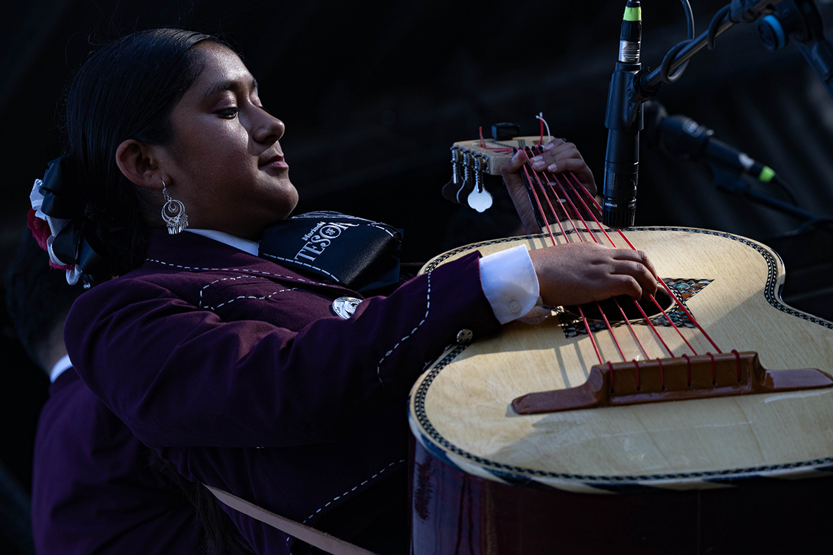 A teenage girl playing the guitarrón, a string instrument that resembles the guitar but has a large, deep body with a rounded back.