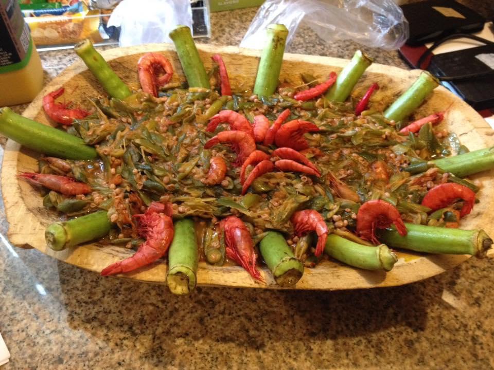 A large wooden dish full of a pureed okra-onion-shrimp mixture, with a “crown” of whole green okra and whole bright red shrimp around the edge. In the middle, there are more shrimp.
