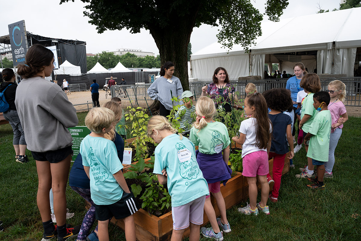 Several young kids and a few adults gather around a garden planter.