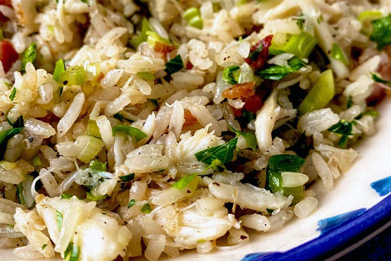 Closeup of rice dish with bits of bacon, crabmeat, and green onions.