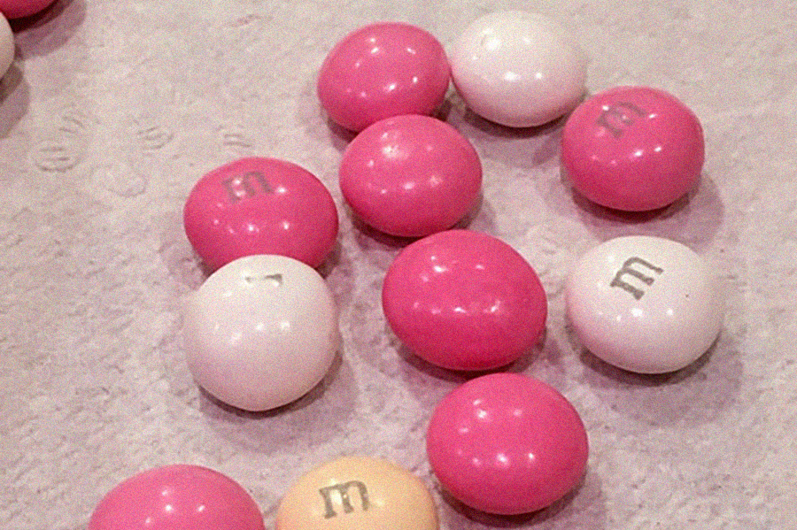 A few pink and white M&Ms, plus one pastel yellow one, scattered on a napkin.