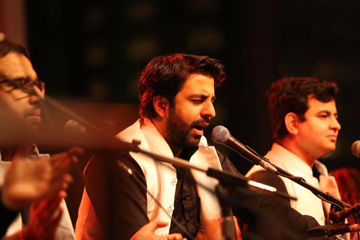 Sonny Mehta of Riyaaz Qawwali, sings into a microphone while drumming.