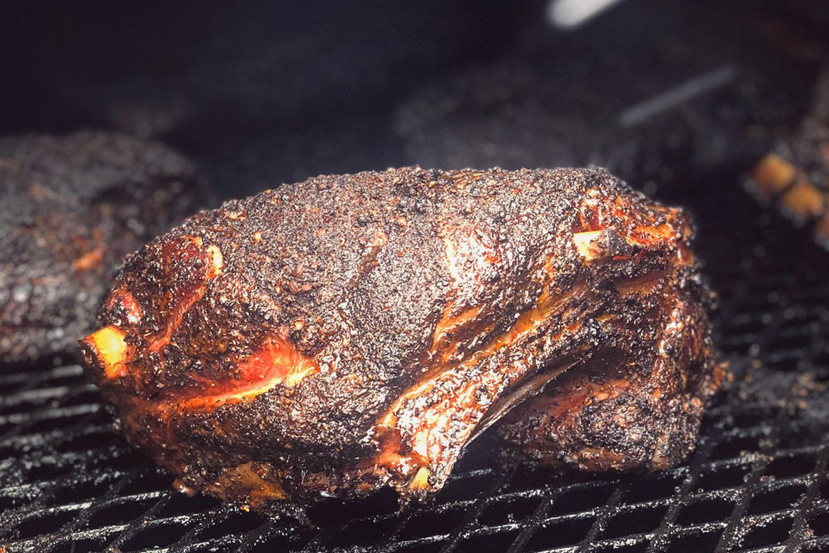 A big hunk of blackened meat on a grill, dark with a thick spice rub.