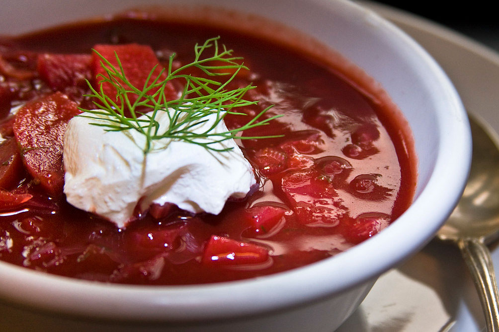 A photo of red borshch in a bowl, garnished with sour cream and dill. 