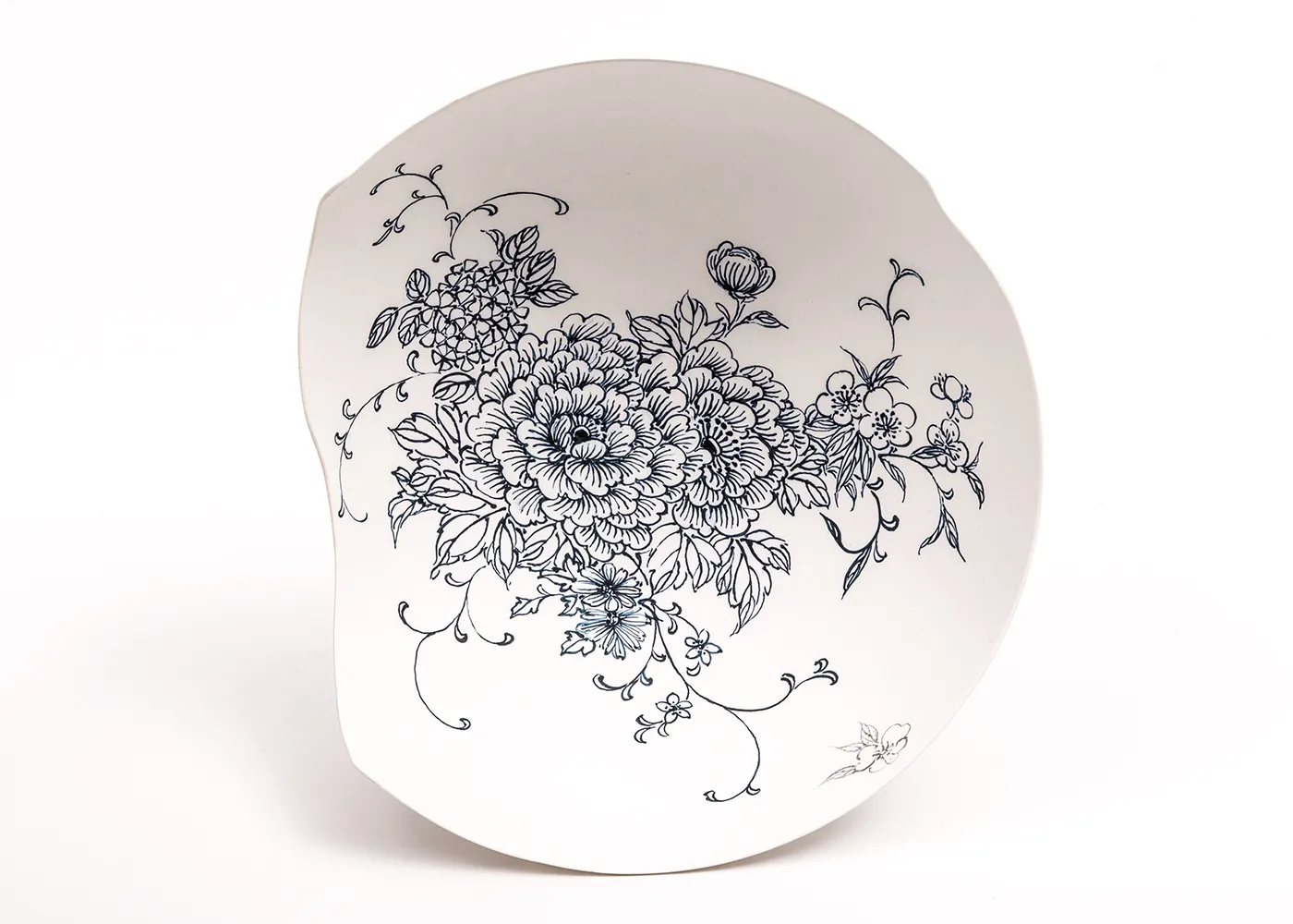 A white asymmetrical bowl with an intricate blue floral design. A small edge piece is missing from the left side of the bowl.   