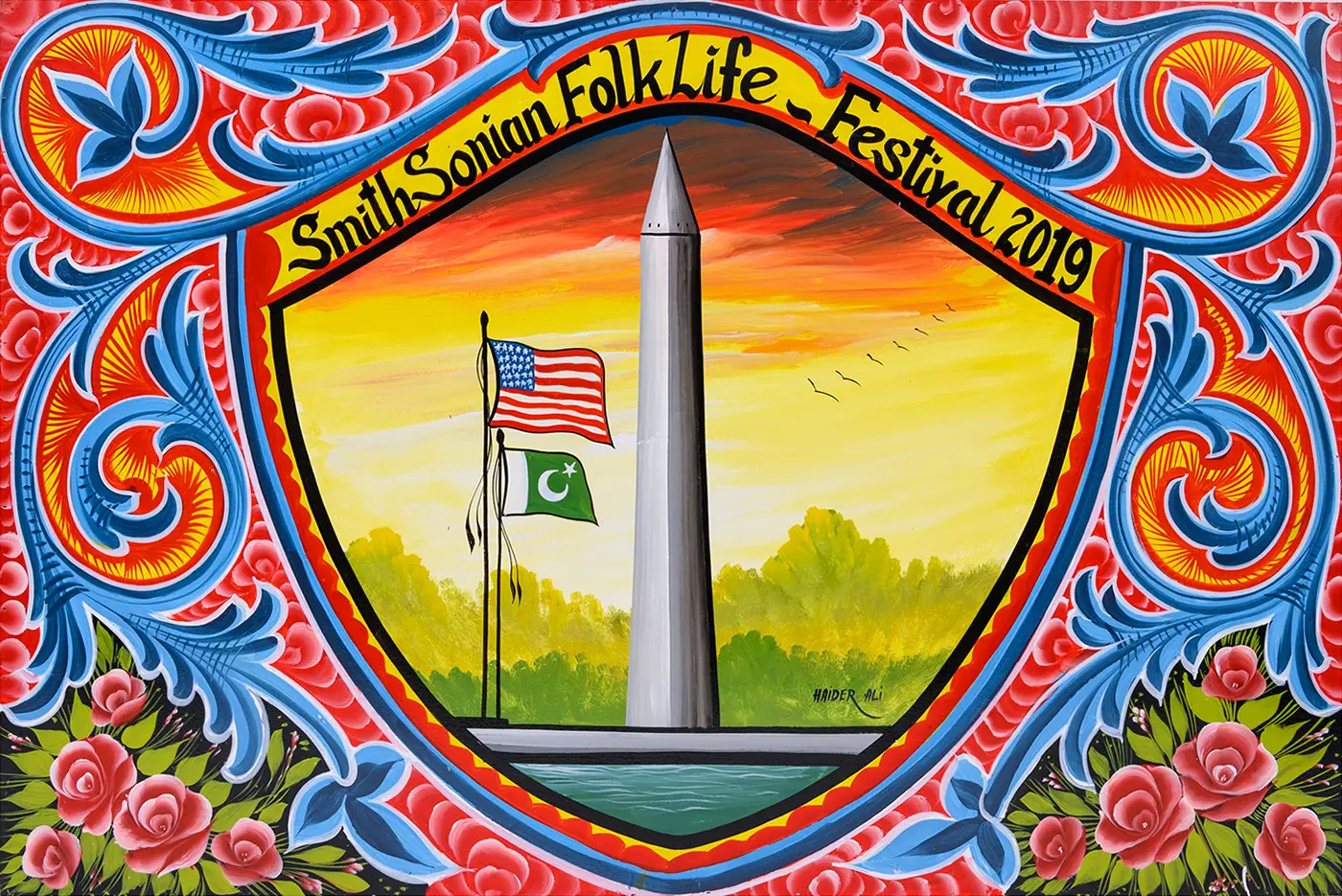 A colorful horizontal painting of the Washington Monument against a yellow and red sky, with two flags flying nearby. A shield-shaped frame surrounds the scene with the words “SmithSonian Folklife Festival 2019” and colorful floral and leaf designs filling the entire surface area.   