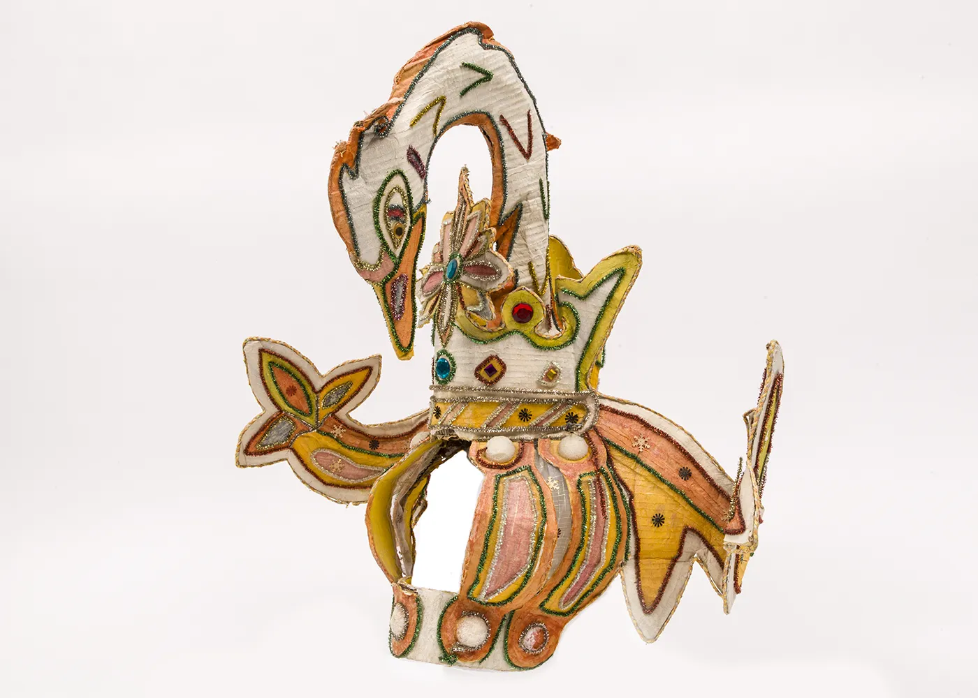 A large white, yellow, and salmon colored headdress ornamented with jewels and tinsel, designed to represent the swooping neck and wings of a swan. 