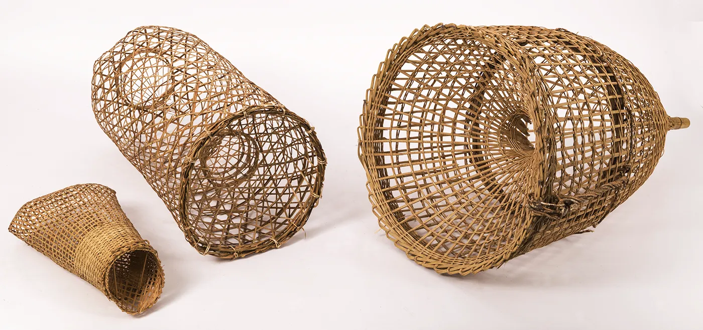 Three fish traps of varying sizes and shapes, intricately woven from light colored bamboo.   