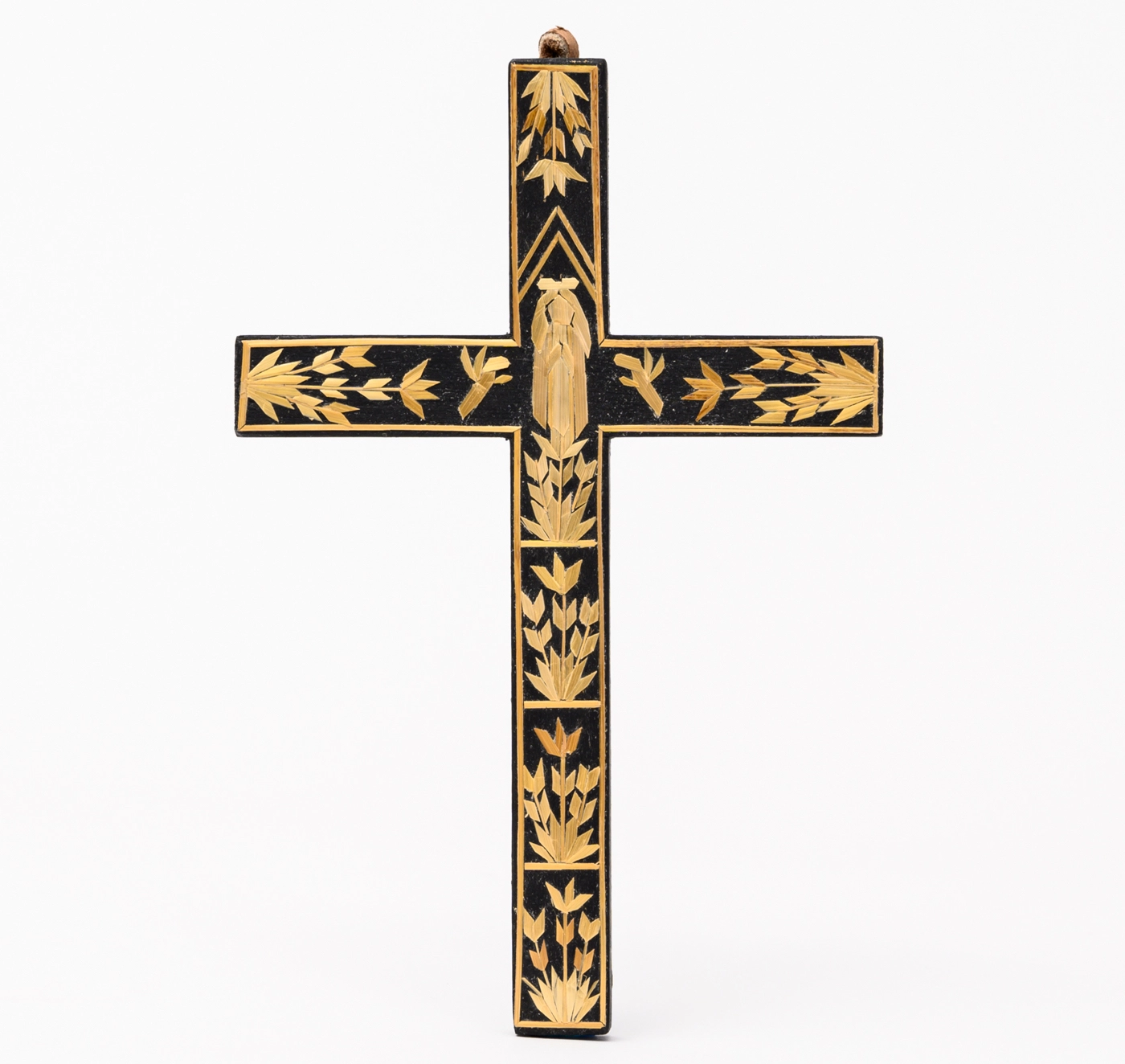 A dark brown wood cross decorated with appliqued straw designs. 