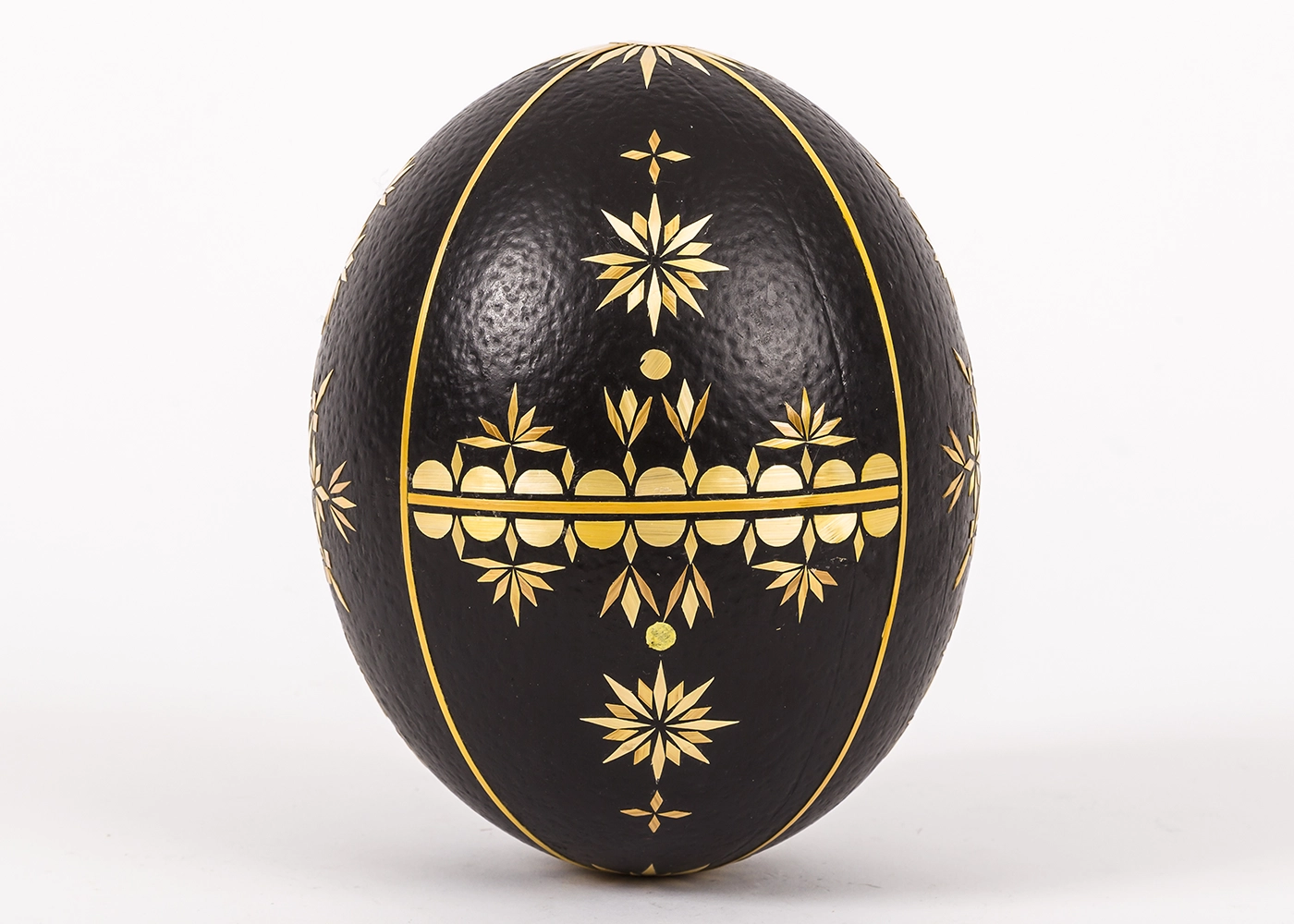 A dark brown ostrich egg standing on its narrow end, decorated with cut-straw designs. 
