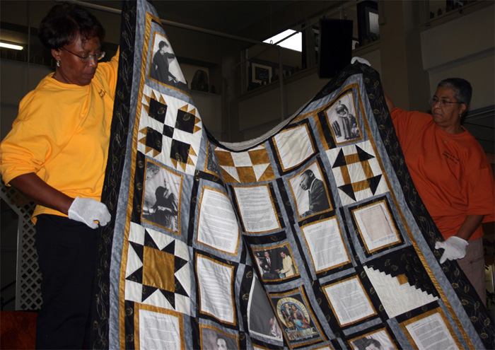 Maxine Stovall and Kathy Muhammad holding an African American history themed quilt made by a member of the Sisters of the Cloth Quilting Guild in Fort Wayne, Indiana. Photo by Jon Kay