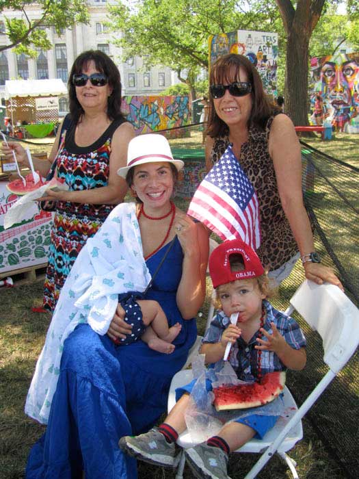 A family enjoys a shady spot and some cool watermelon in the tree plot by the Citified Festival program. Photo by Patricia Wakida