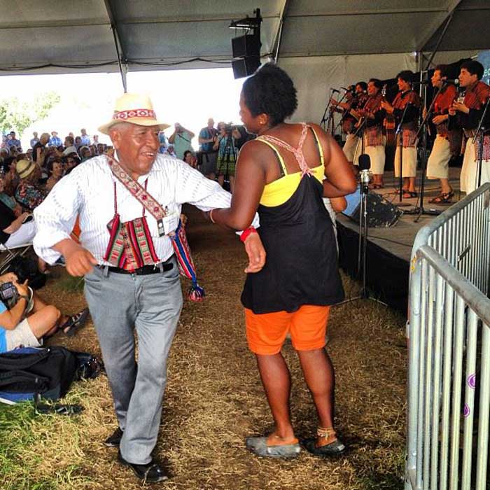 Arlean Dawes dances with Walter Alvarez, a Kallawaya medicinal expert from Bolivia, while Los Masis performs on the Voices of the World stage. Photo by Karon Flage