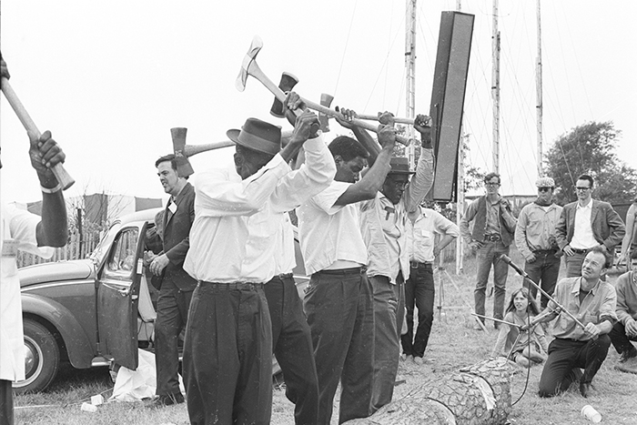 A Texas work song group performs at the 1965 Newport Folk Festival. Alan Lomax stands by the car at left, and Pete Seeger is holding a microphone at right. The singers are: Rufus Williams, Lee Protho, Charlie Coleman, Andrew Crane, and Alfred Paul East.