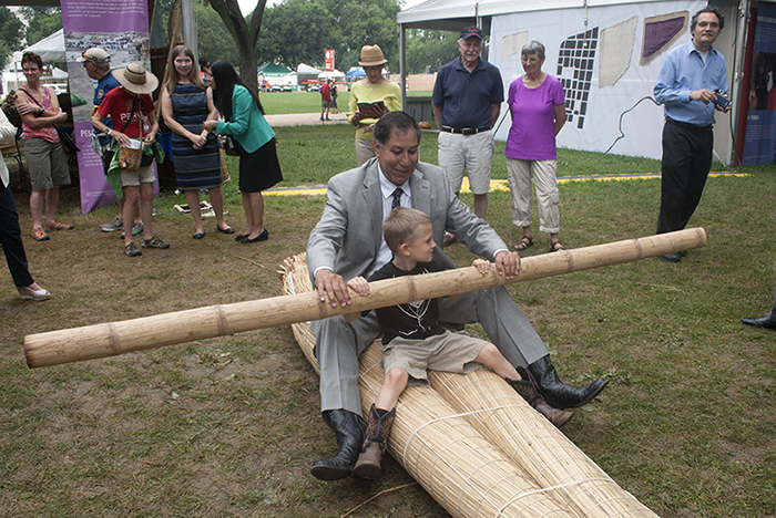 Ed Avalos, the Undersecretary of Marketing at the U.S.D.A., helped a young visitor learn to ride a <em>caballito de totora</em> raft. Photo by J.B. Weilepp, Ralph Rinzler Folklife Archives