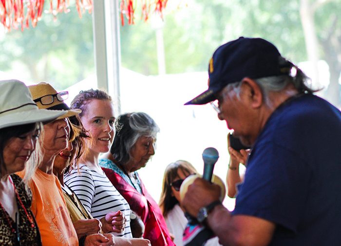 An older man with a microphone faces a line of people.