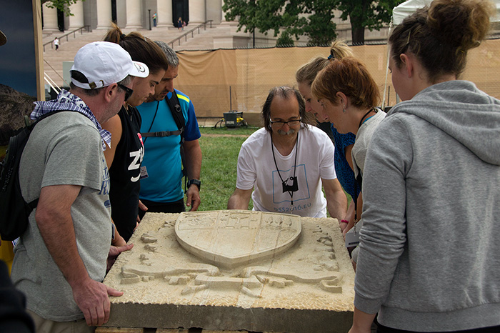 The Basque rural sports athletes admire the stone work of Bernat Vidal, who has been chipping away at this piece since Wednesday. Photo by Gregory Gottlieb, Ralph Rinzler Folklife Archives