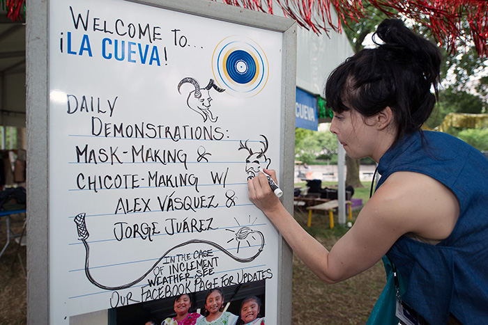 Each morning, Folklife Festival staff updates the daily schedules on whiteboard signs. Here's <em>Sounds of California</em> intern Katie Radishofski adding some <em>diablos</em> illustrations to La Cueva. Photo by Walter Larrimore, Ralph Rinzler Folklife Archives