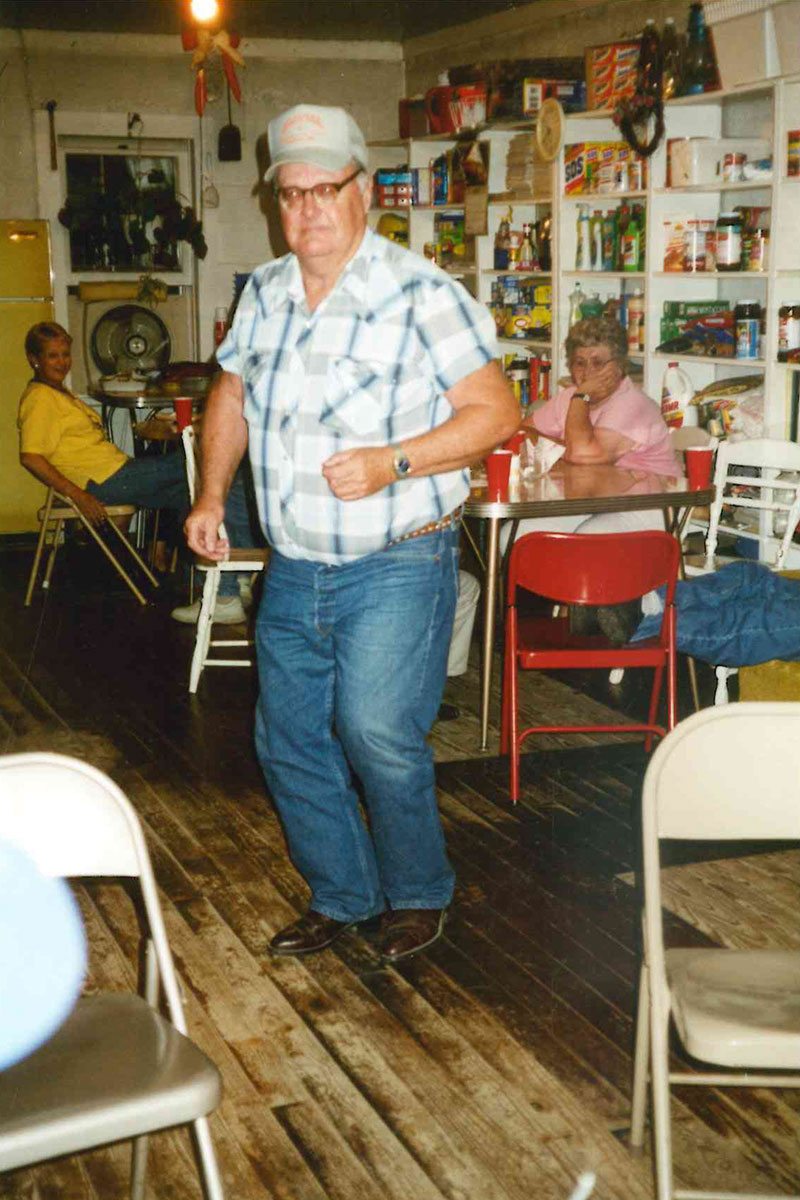 A man dances among folding chairs and seated people in a home.