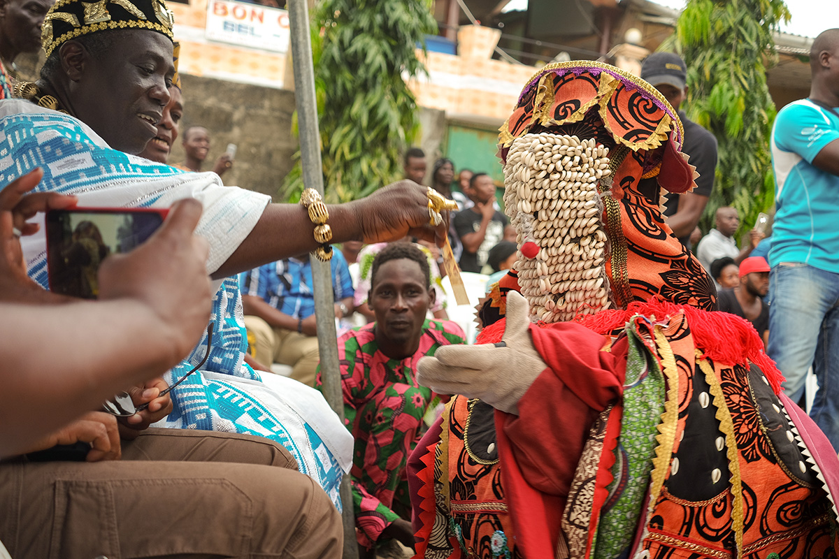 Dancemaker Koffi Alade interacts with an Egungun, a cloth masquerade embodying an ancestor, at a community performance near Cotonou, Benin.