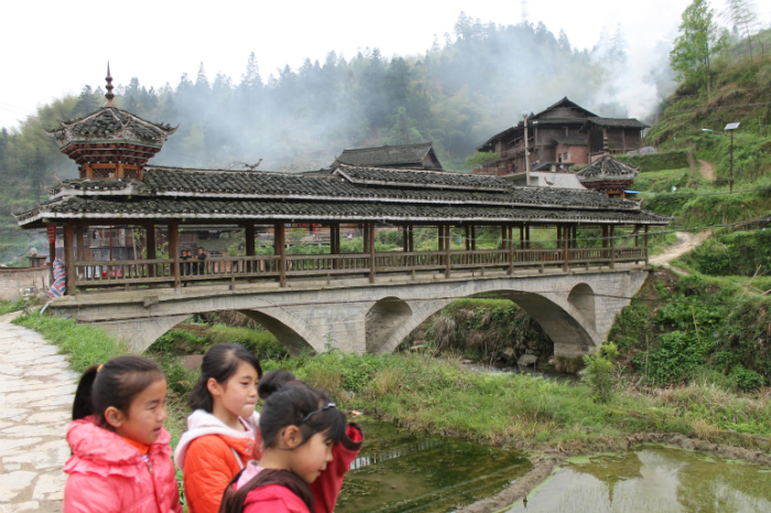 The “Wind and Rain” covered wooden bridge in Dimen is a characteristic Dong village architectural feature, typically with built-in resting spots at either end. A few minutes earlier the three girls were afraid of me, then their curiosity prevailed. Photo by Atesh Sonneborn