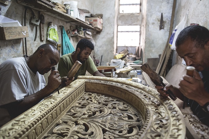 Kenyan wood carvers work on a decorative piece for over a door.